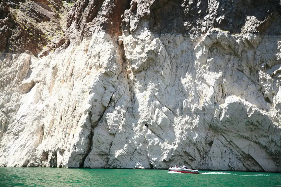A pale mineral band roughly a hundred feet tall exposed on the rock wall above the waterline at Lake Mead, with a small motorboat below it for scale.